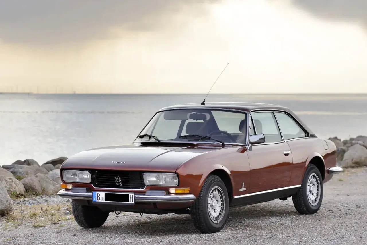 Brun Peugeot 504 coup&eacute; parkerad vid havet. En klassisk bil med tidl&ouml;s design.