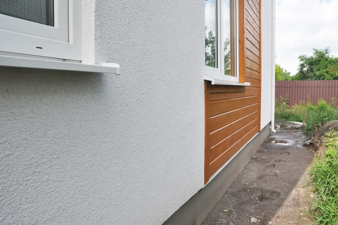 Nytt hus med vit puts och träpanel. Grunden ovan mark är isolerad för att skydda mot kyla.