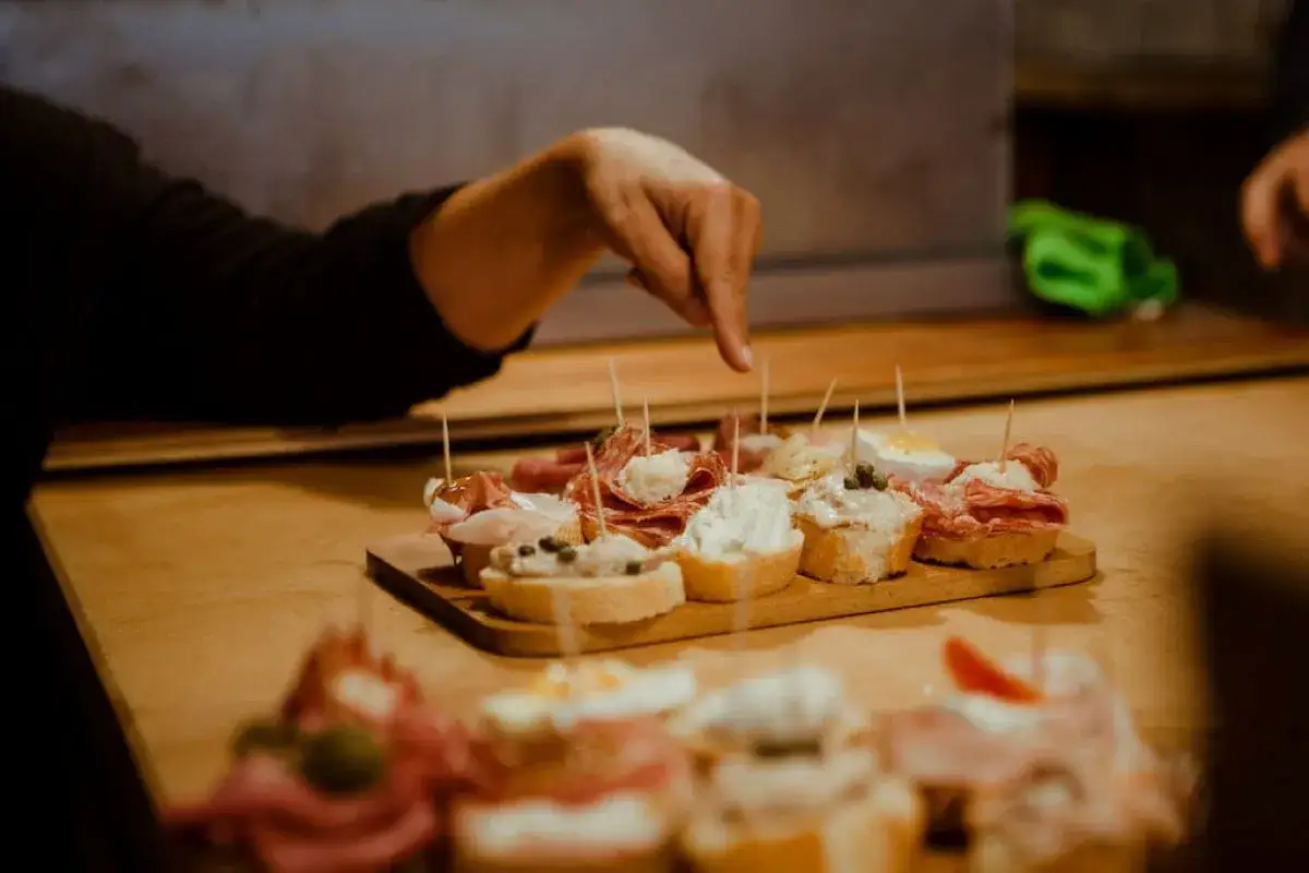 Main d'une personne choisissant parmi des **cantine del vino gi&agrave; schiavi** : de d&eacute;licieux petits toasts garnis de charcuterie et de fromage.