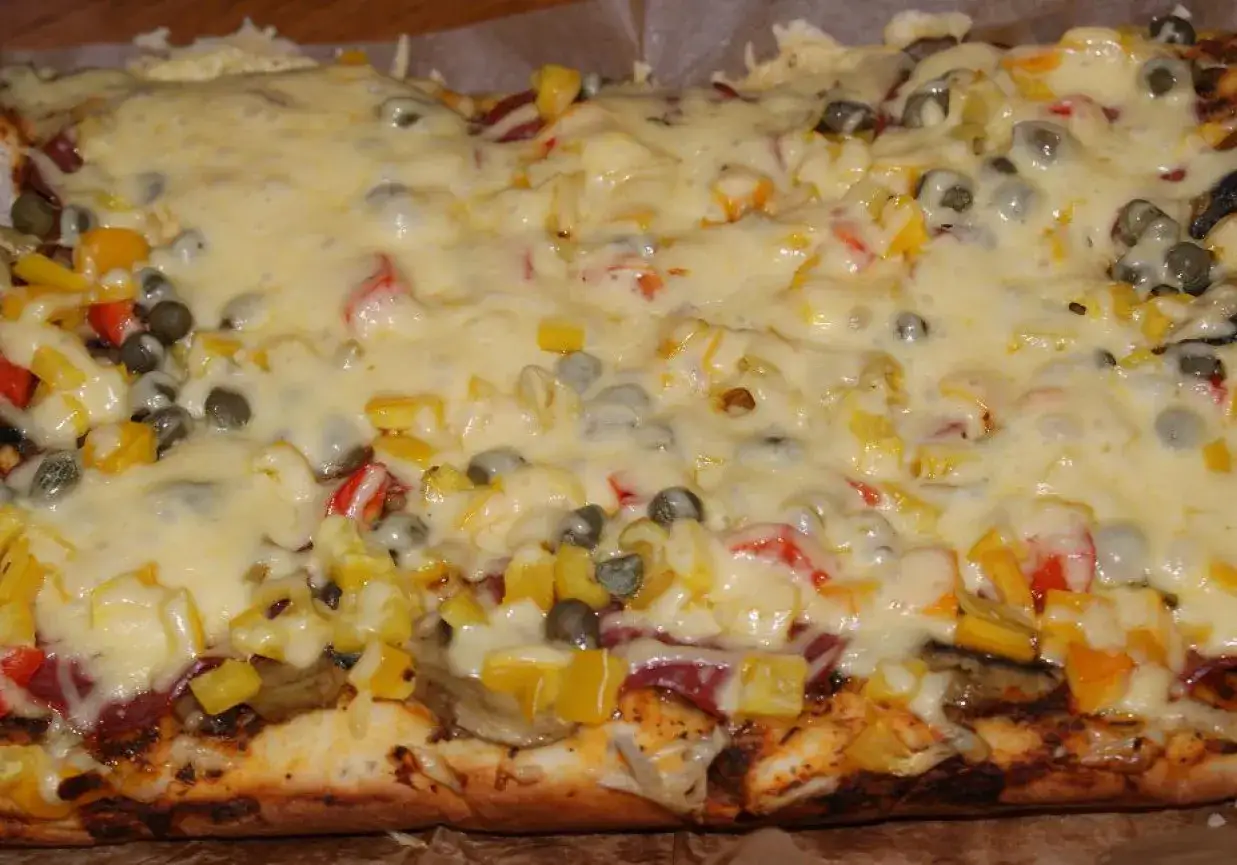 Pyszna pizza na grubym cieście z warzywami i roztopionym serem.