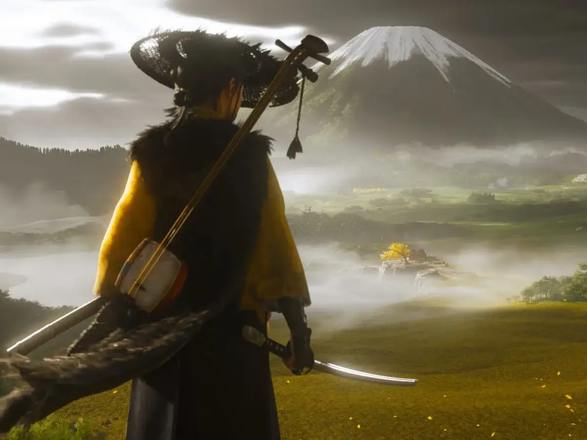 Un samurái con un shamisen a la espalda y una katana en mano, contemplando un paisaje brumoso con el monte Fuji al fondo. Guía Ghost of Yotei.