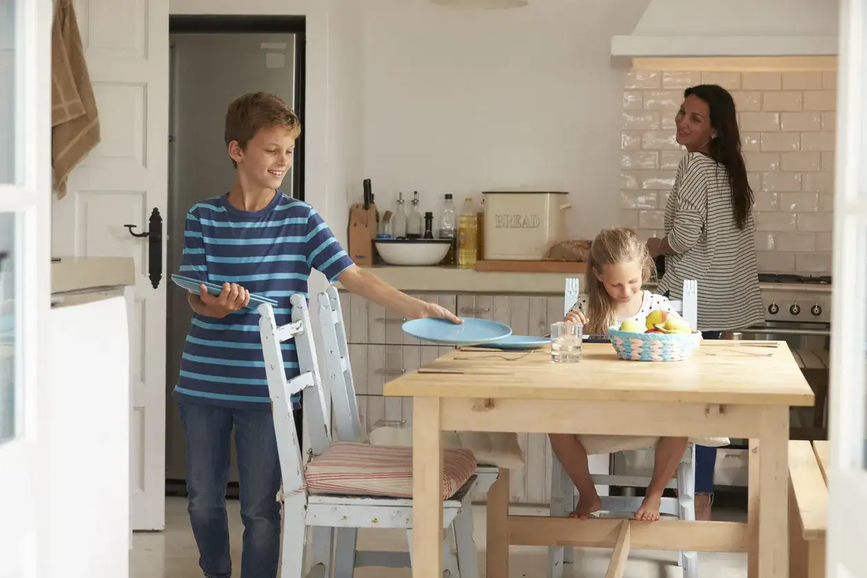 Un niño de 7 años ayuda a poner la mesa en la cocina, mientras su hermana y su madre observan.