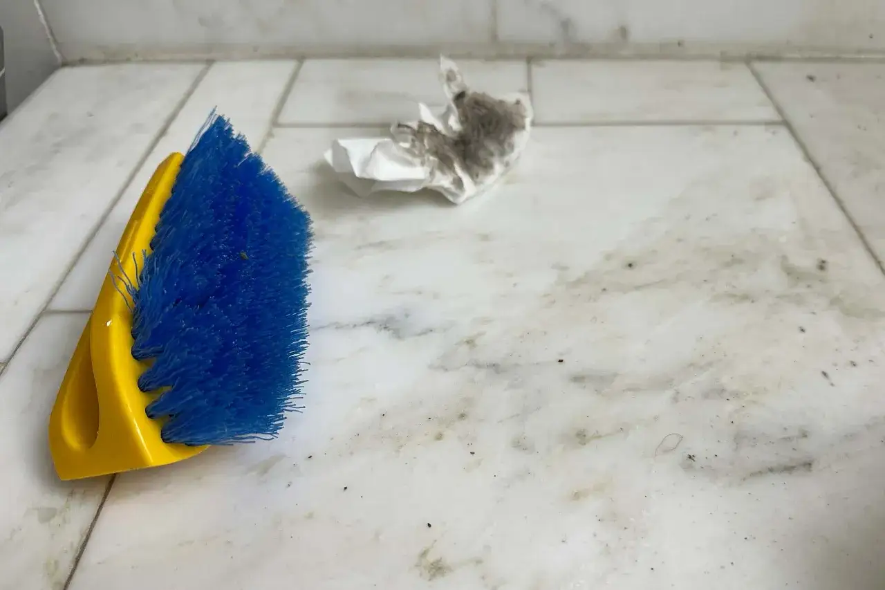 Brosse bleue et jaune prête à nettoyer sol carrelage très sale. Un mouchoir plein de poussière est à côté.