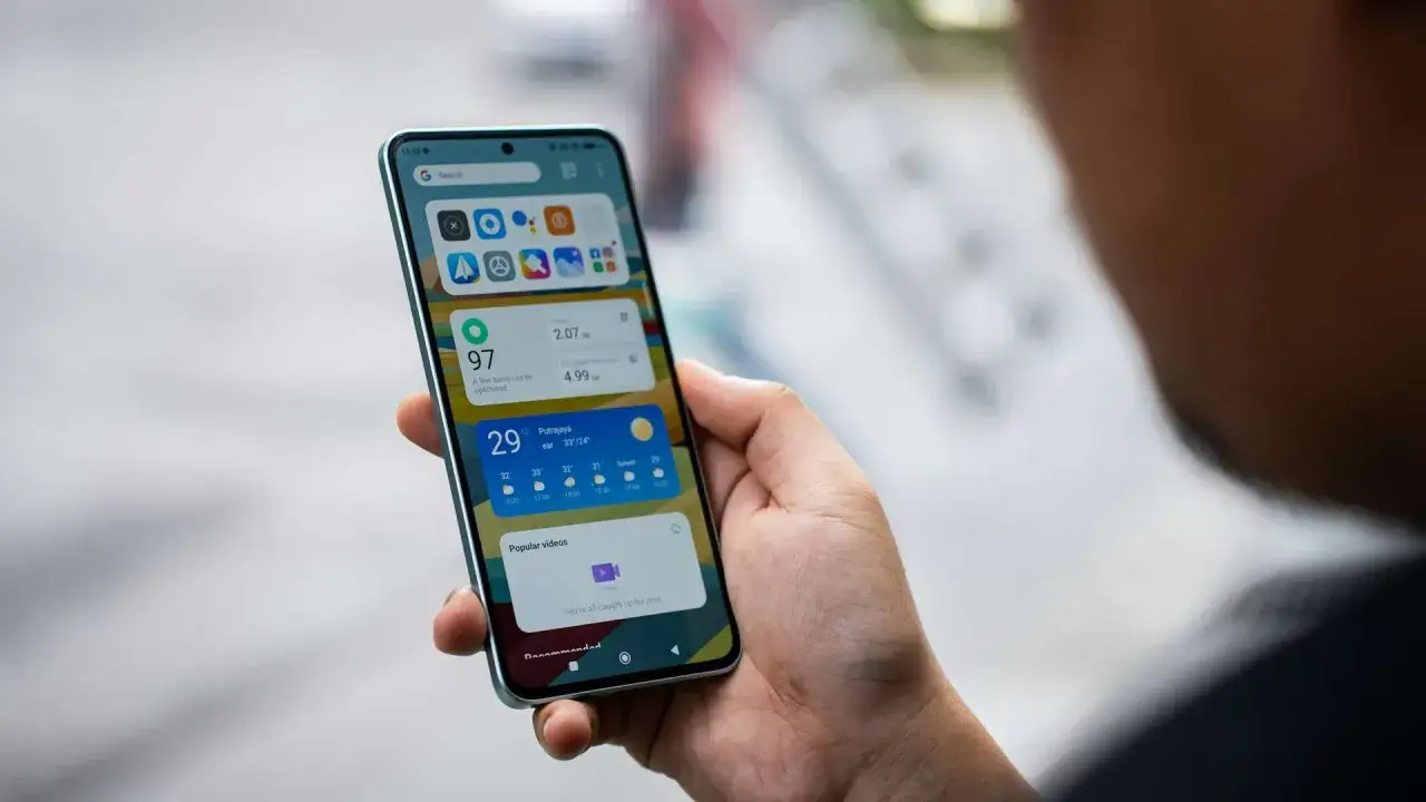 Dłoń trzyma smartfon z widżetami, w tym pogodą i informacjami o optymalizacji. Ułatwia to **online check-in** do usług.