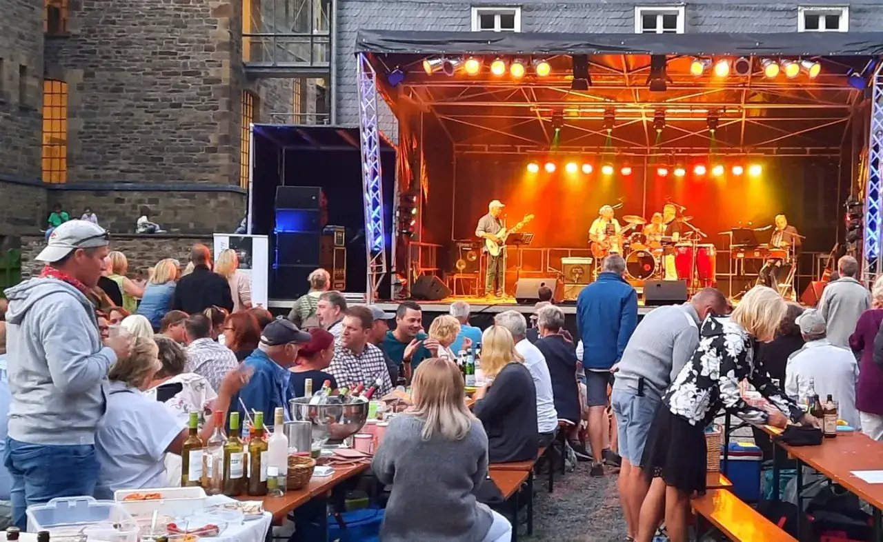 Live-Musik auf der B&uuml;hne, Menschen sitzen an Tischen und genie&szlig;en das Abendessen. Ein tolles Event in Engelskirchen heute!