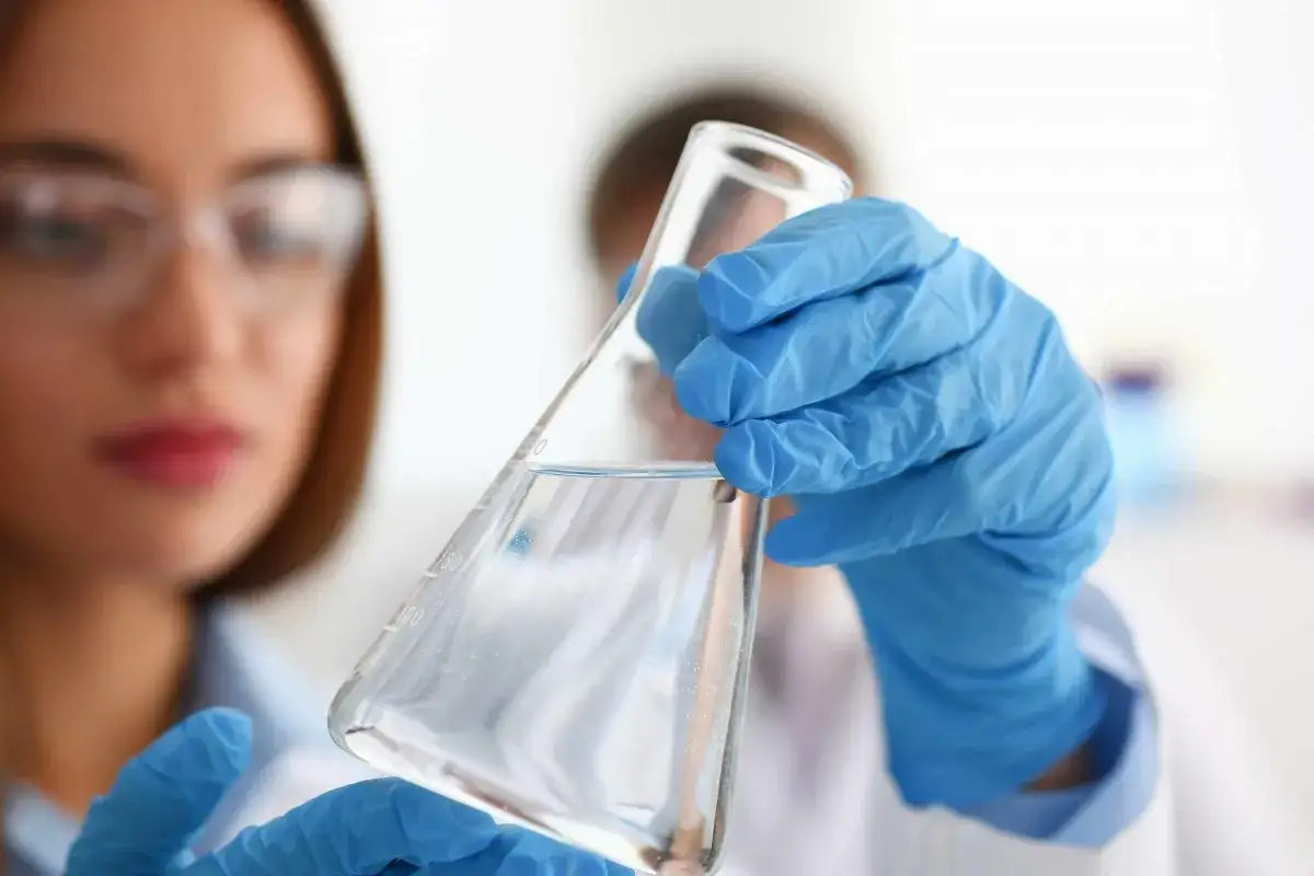 Scientifique en blouse et gants bleus examine un erlenmeyer rempli d'eau à boire pure, gage de santé.