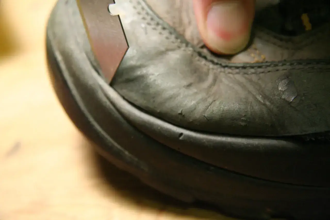 A razor blade is used to separate the sole of a worn boot, showing the sole of boot coming off.