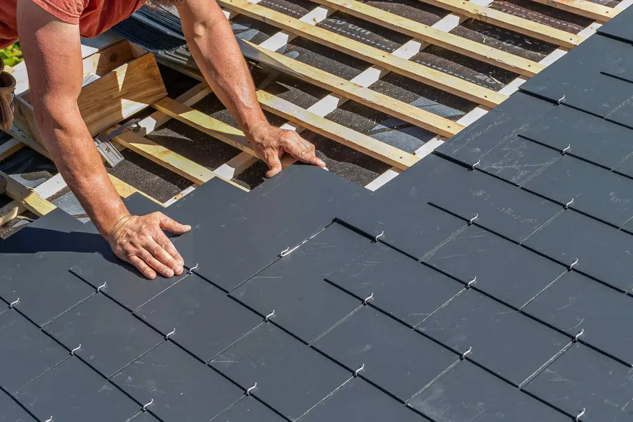 Dachdecker verlegt Schieferplatten. Die Sanierung eines Eternit Daches kann kostenintensiv sein, aber moderne Alternativen sind langlebig.