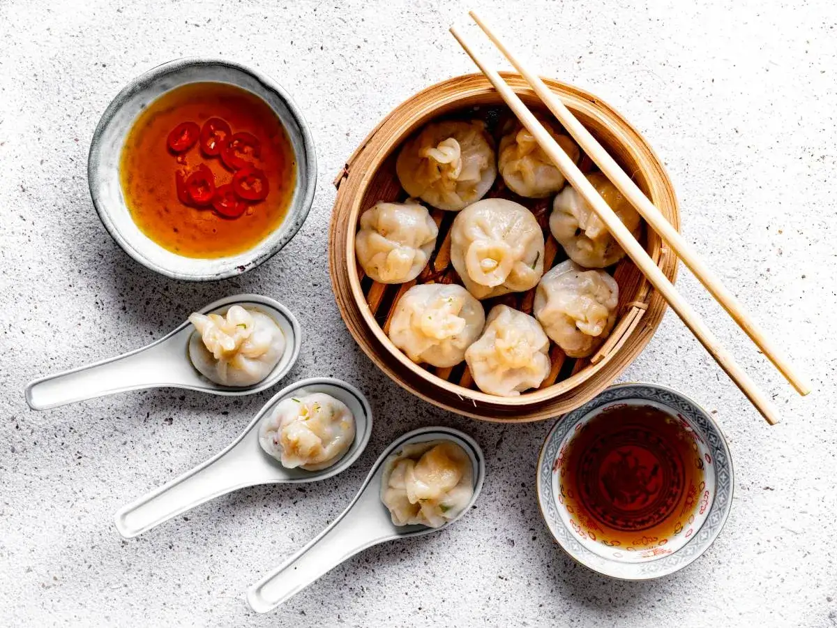 Pierożki dim sum w bambusowym parowniku, podane z sosem chili i sosem sojowym.