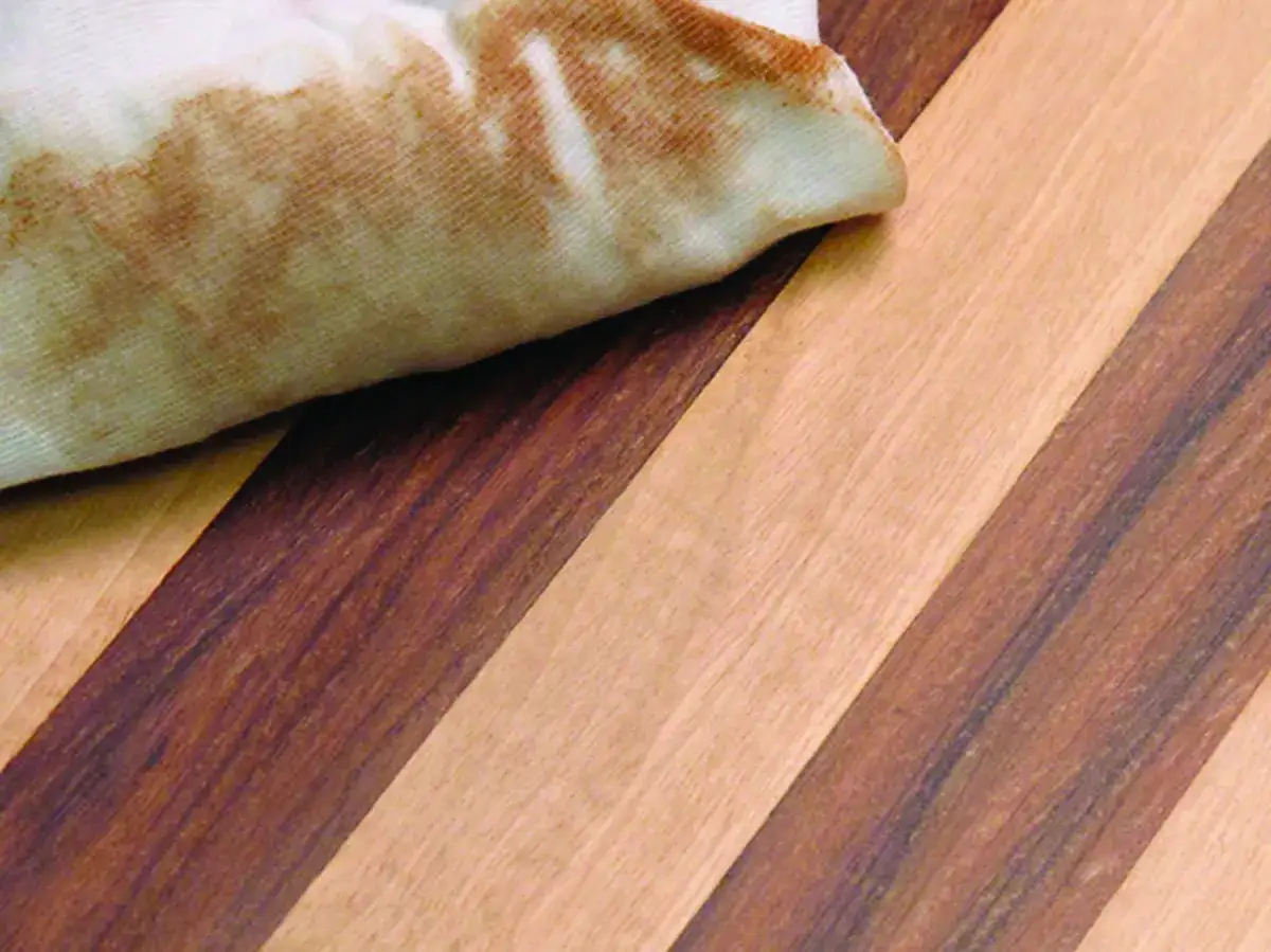 Chiffon imbib&eacute; d'ac&eacute;tone pour d&eacute;graisser bois, sur un fond de lamelles de bois contrast&eacute;es.