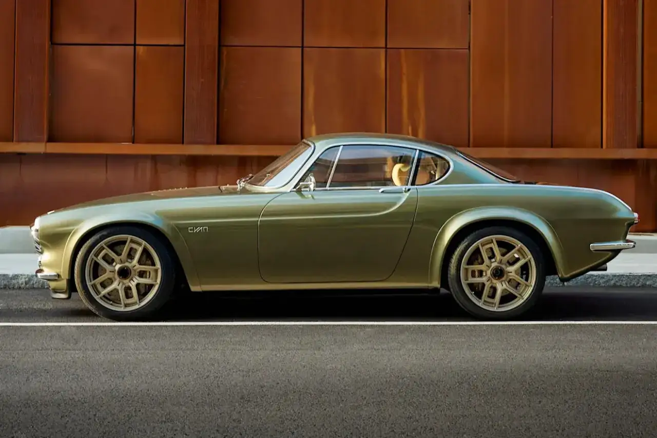 Elegancki, oliwkowy Volvo P1800 z lat 60. na złotych felgach, zaparkowany na tle rustykalnej, miedzianej ściany.