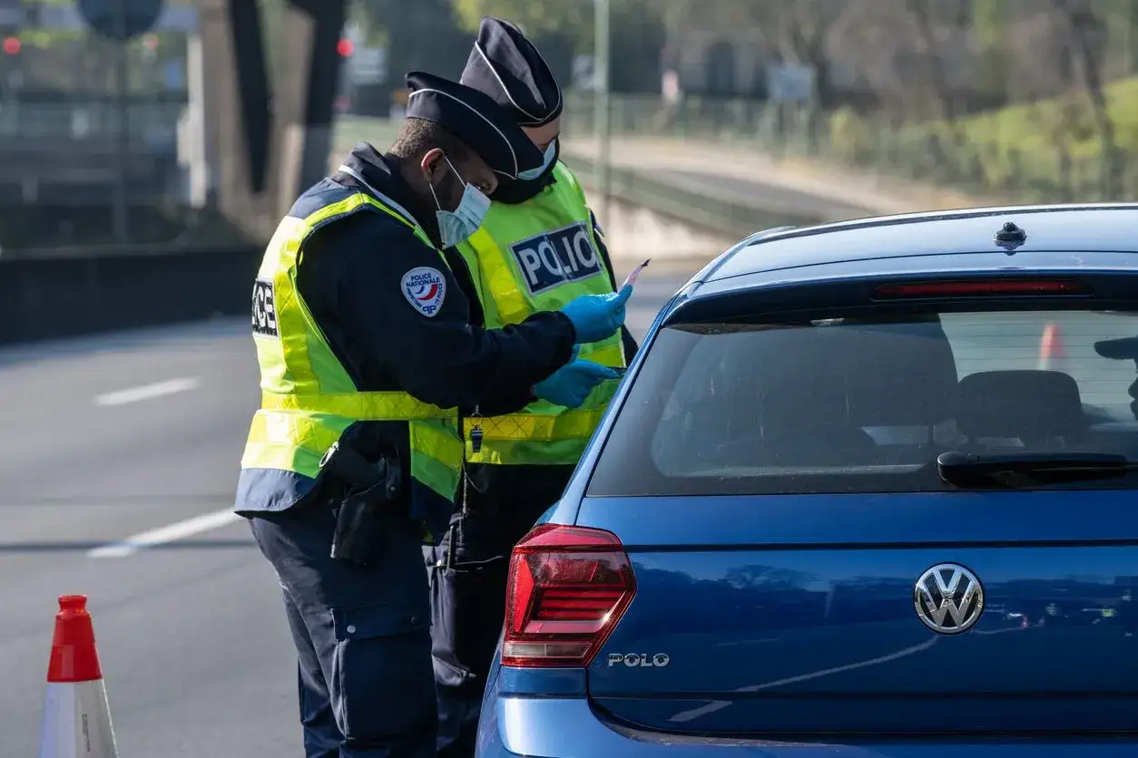 Deux policiers contrôlent un véhicule. L'un d'eux semble vérifier des papiers, peut-être un cas de défaut d'assurance 6 points.