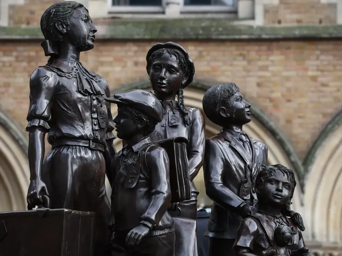 Statue de bronze commémorant les enfants sauvés par Nick Winton, portant des étiquettes d'identification, prêts pour un nouveau départ.