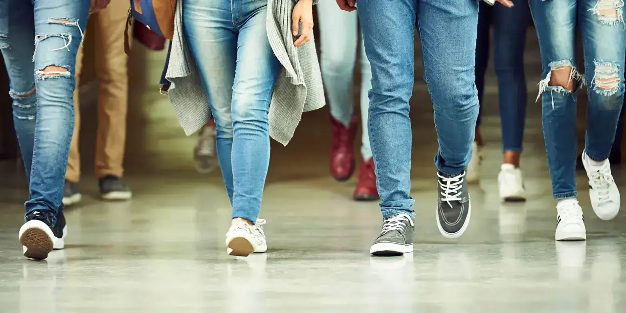 Ungdomar i jeans och sneakers går i en korridor. Kanske på väg till en lektion med fri kvot gymnasiet.