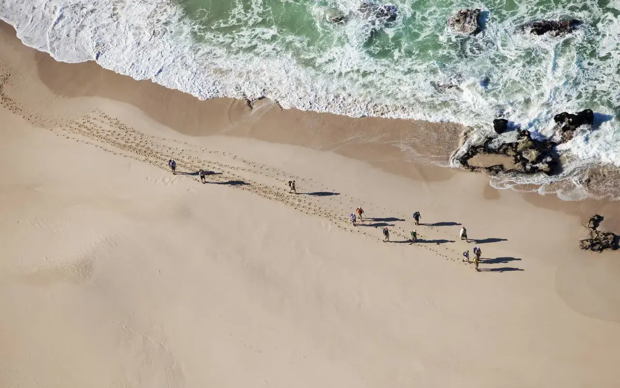 Wanderer hinterlassen Spuren am Strand des De Hoop Nature Reserve, während die Wellen sanft anrollen.