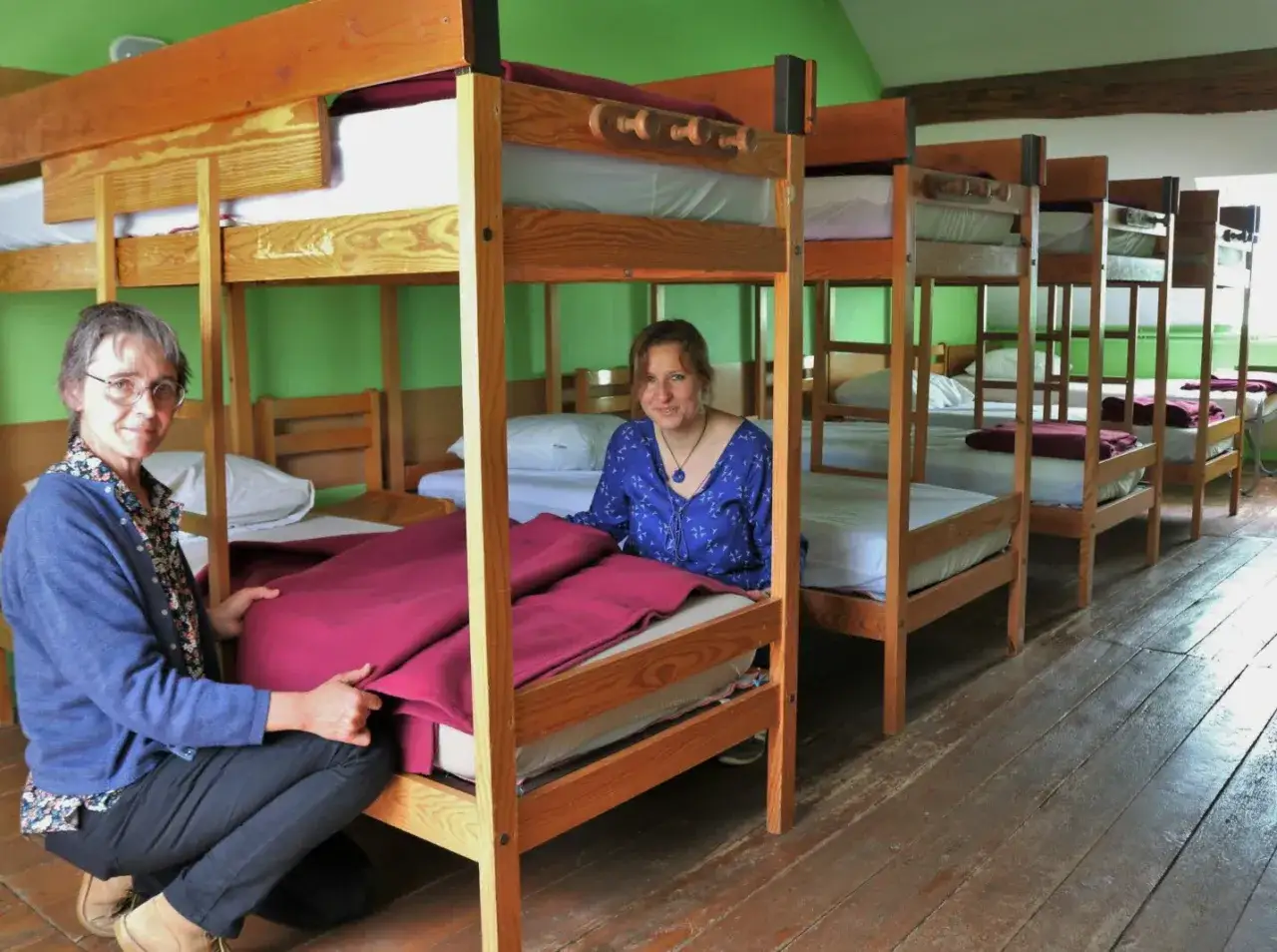 Deux femmes préparent un dortoir colonie de vacances avec des lits superposés en bois.