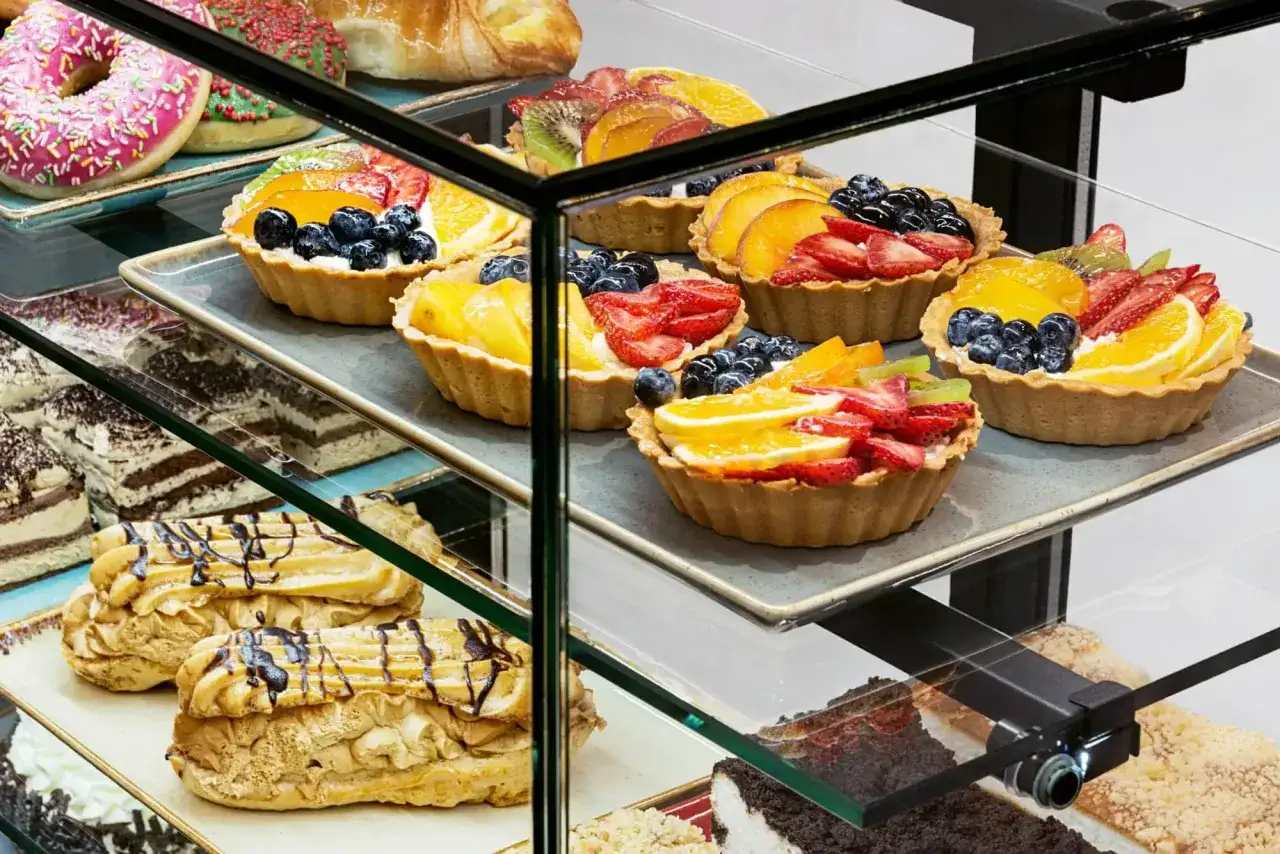 Kolorowe babeczki z owocami, pączki i eklerki kuszą w witrynie cukierni. Zastanawiasz się, ile kosztuje kg ciasta?