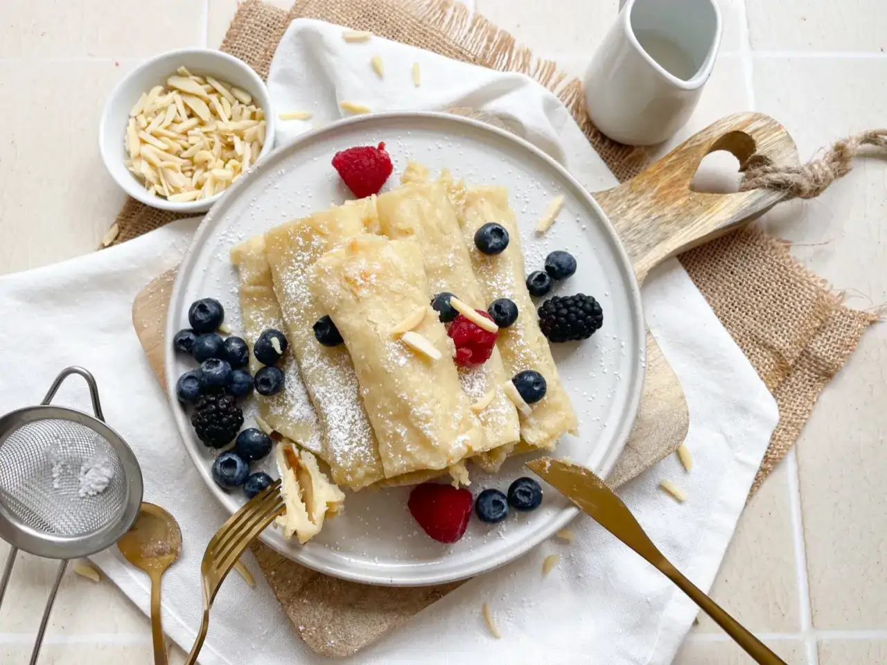 Leckere, gerollte Pfannkuchen ohne Ei, bestäubt mit Puderzucker und garniert mit Beeren und Mandelblättchen.