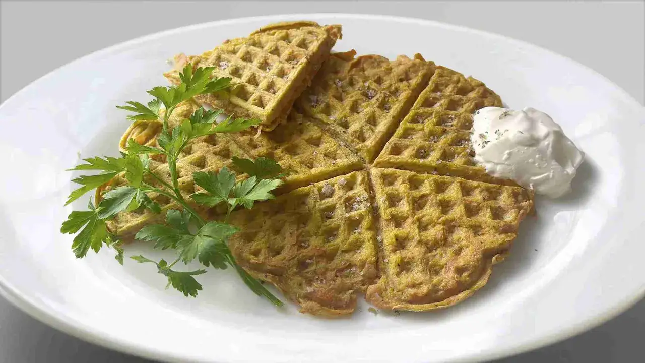 Herzhafte karotten waffeln, goldbraun gebacken, mit frischer Petersilie und einem Klecks Dip serviert.