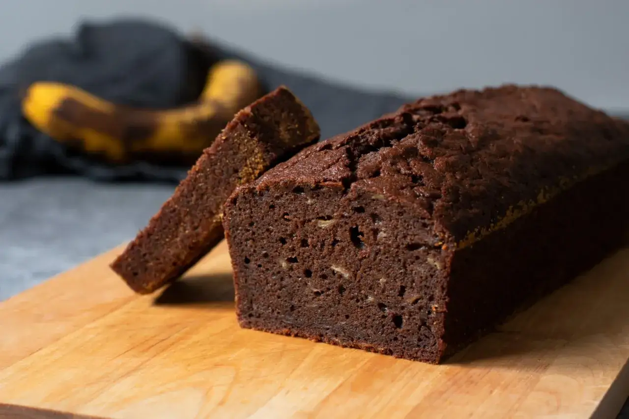 Chokladig banankaka, perfekt för ett enkelt banankaka recept. En skiva är uppskuren och en övermogen banan ligger i bakgrunden.