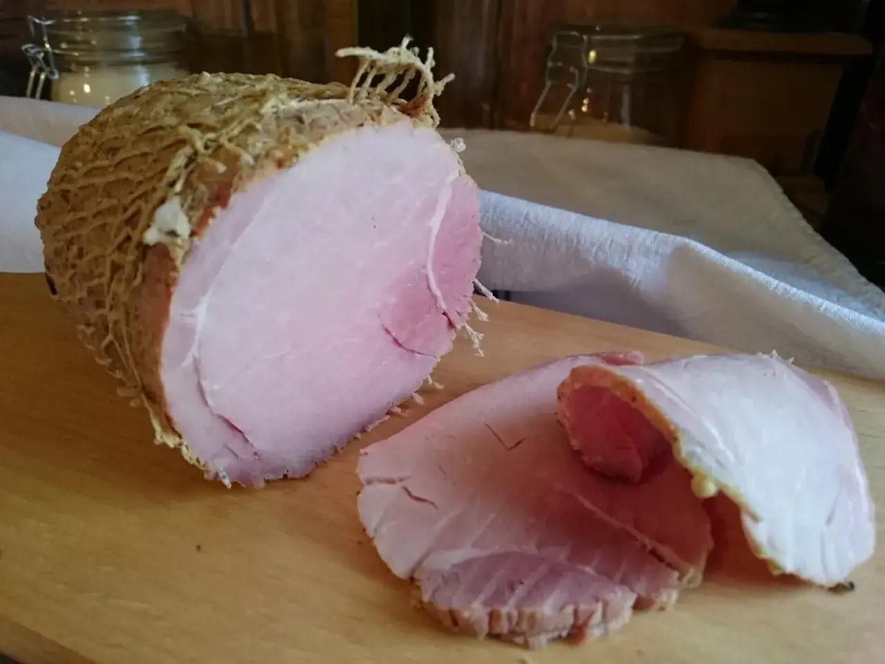 Pyszna szynka po peklowaniu, gotowa do krojenia. Widać jej soczyste, różowe mięso i delikatną skórkę.