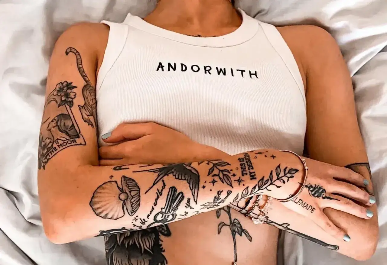 Arme mit vielen kleinen Tattoos im Stil von Illustrationen, darunter eine Muschel, ein Vogel und Pflanzen.