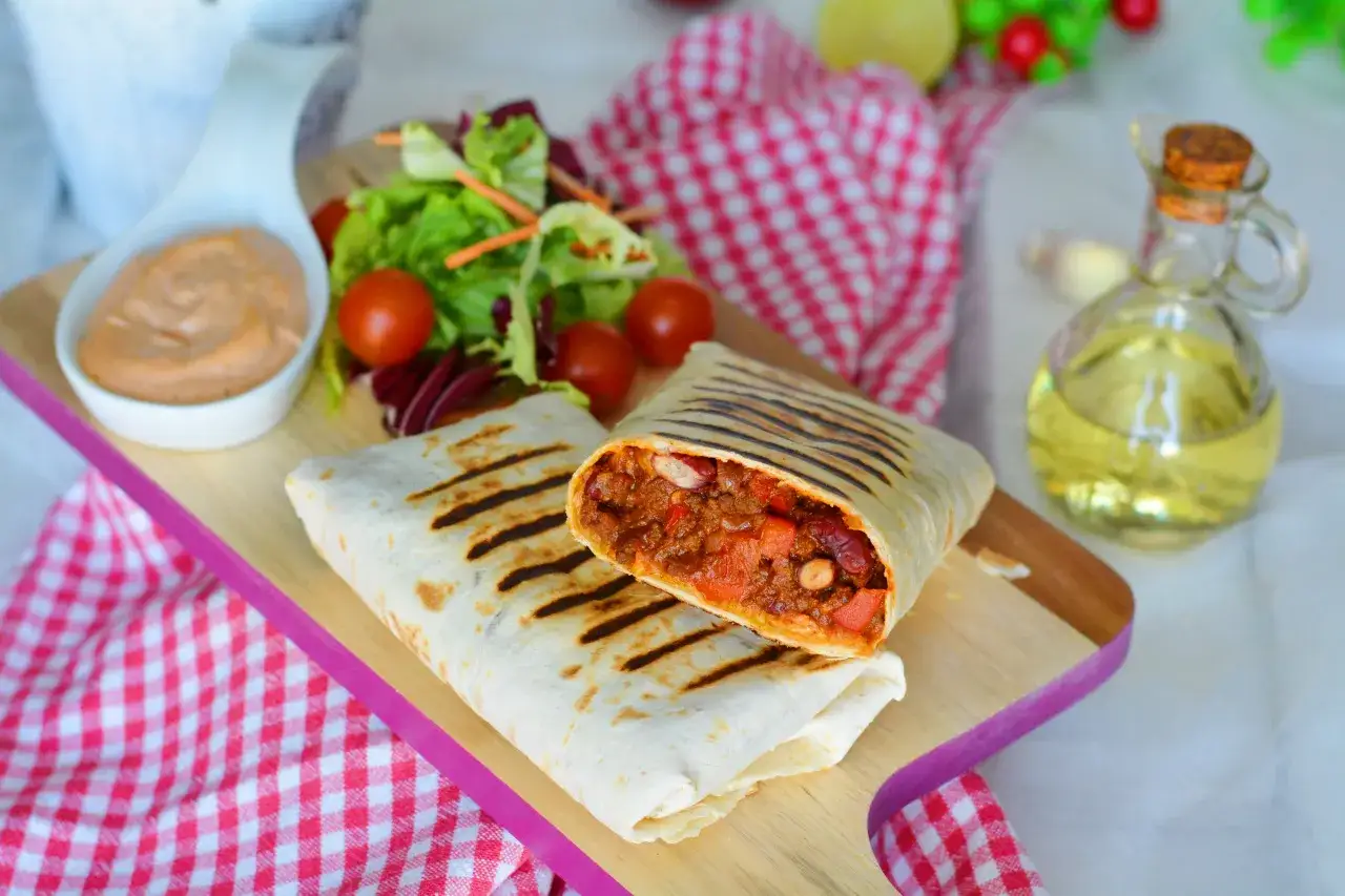 Pyszny burrito przepis na talerzu: grillowane tortille z aromatycznym farszem mięsnym, fasolą i warzywami, podane z sałatką i sosem.