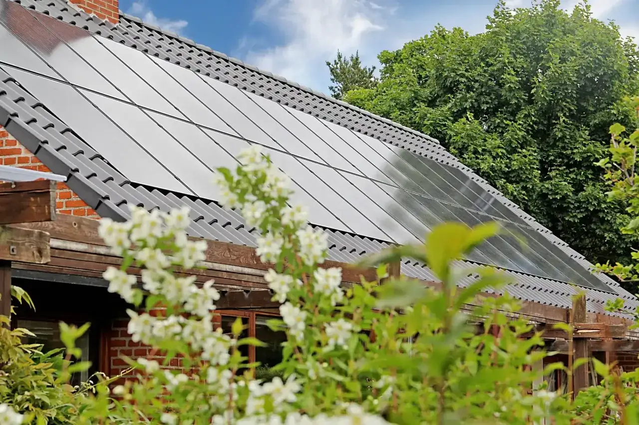 Tak p&aring; ett hus med solceller som bidrar till solceller h&aring;llbarhet. Blommor i f&ouml;rgrunden.