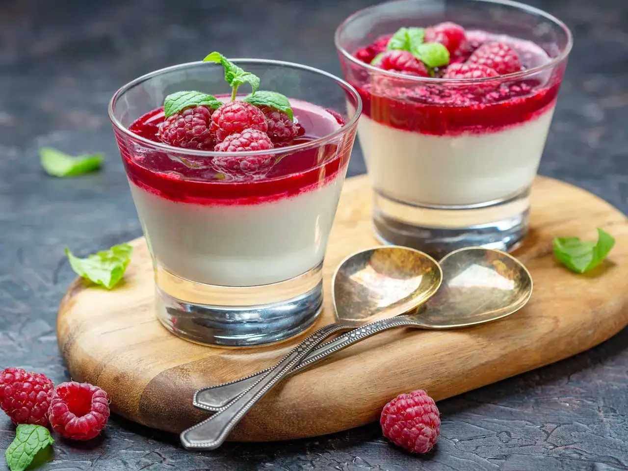 D&eacute;licieux panna cotta yaourt aux framboises fra&icirc;ches et menthe, servi dans des verres sur une planche en bois.