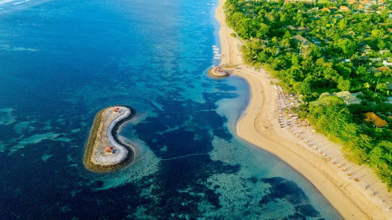 Sanur Bali: En lugn strand med turkost vatten, små tempel på stenpirar och grönskande vegetation.