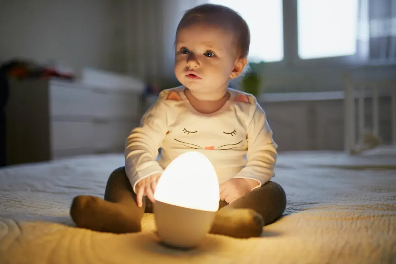 Urocza lampka do pokoju dziecka rozświetla twarz malucha.