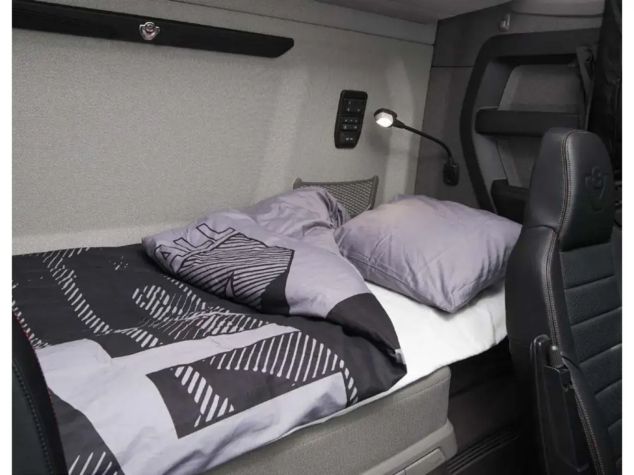 L'int&eacute;rieur d'une cabine camion luxe avec un lit confortable, une couette moderne et un oreiller. Une lampe de lecture est fix&eacute;e au mur.