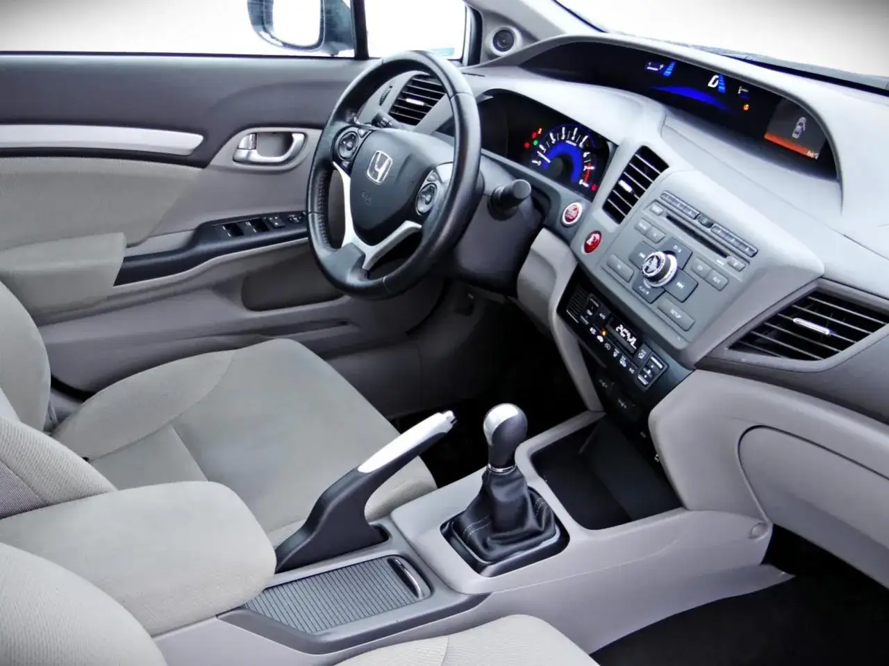 Wnętrze honda civic sedan: kierownica, deska rozdzielcza z wyświetlaczem, dźwignia zmiany biegów i jasne siedzenia.