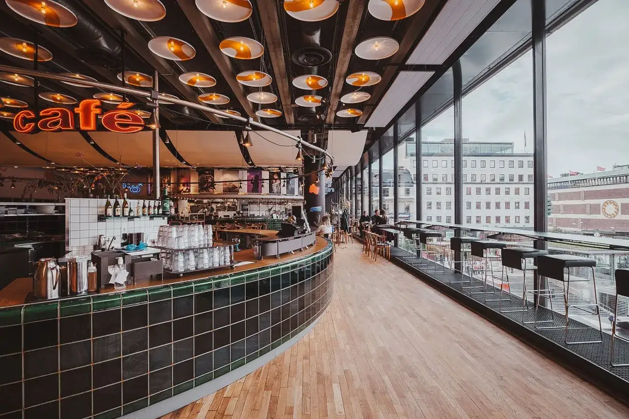 Mysig caféinredning med neonljus och stora fönster med utsikt över stadens takåsar. En perfekt plats att koppla av på vid kulturhuset i Stockholm.