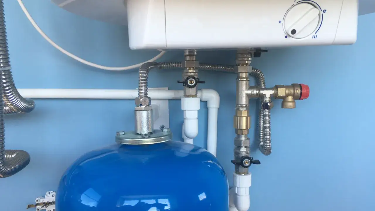 D&eacute;tail de la plomberie d'un chauffe-eau, avec un r&eacute;servoir bleu et des tuyaux m&eacute;talliques. Un guide pour choisir son chauffe eau.