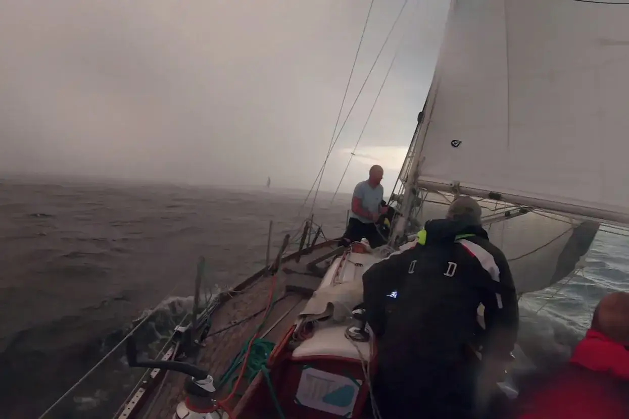 Un voilier affronte un **orage de mer**, les vagues s'écrasent sur le pont tandis que l'équipage lutte contre les éléments.