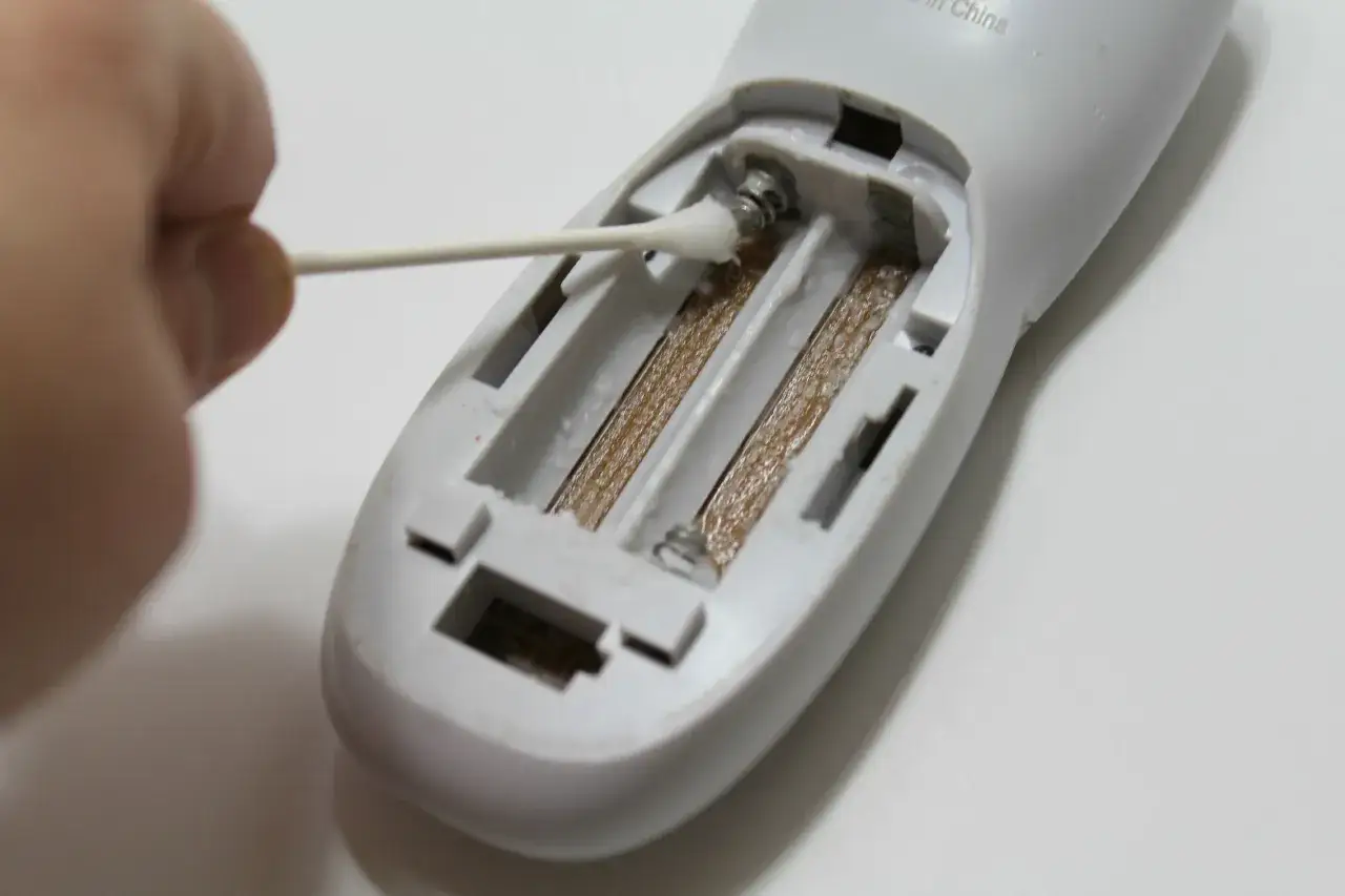 Mit einem Wattestäbchen wird ausgelaufene Batterie im Batteriefach eines Geräts gereinigt.