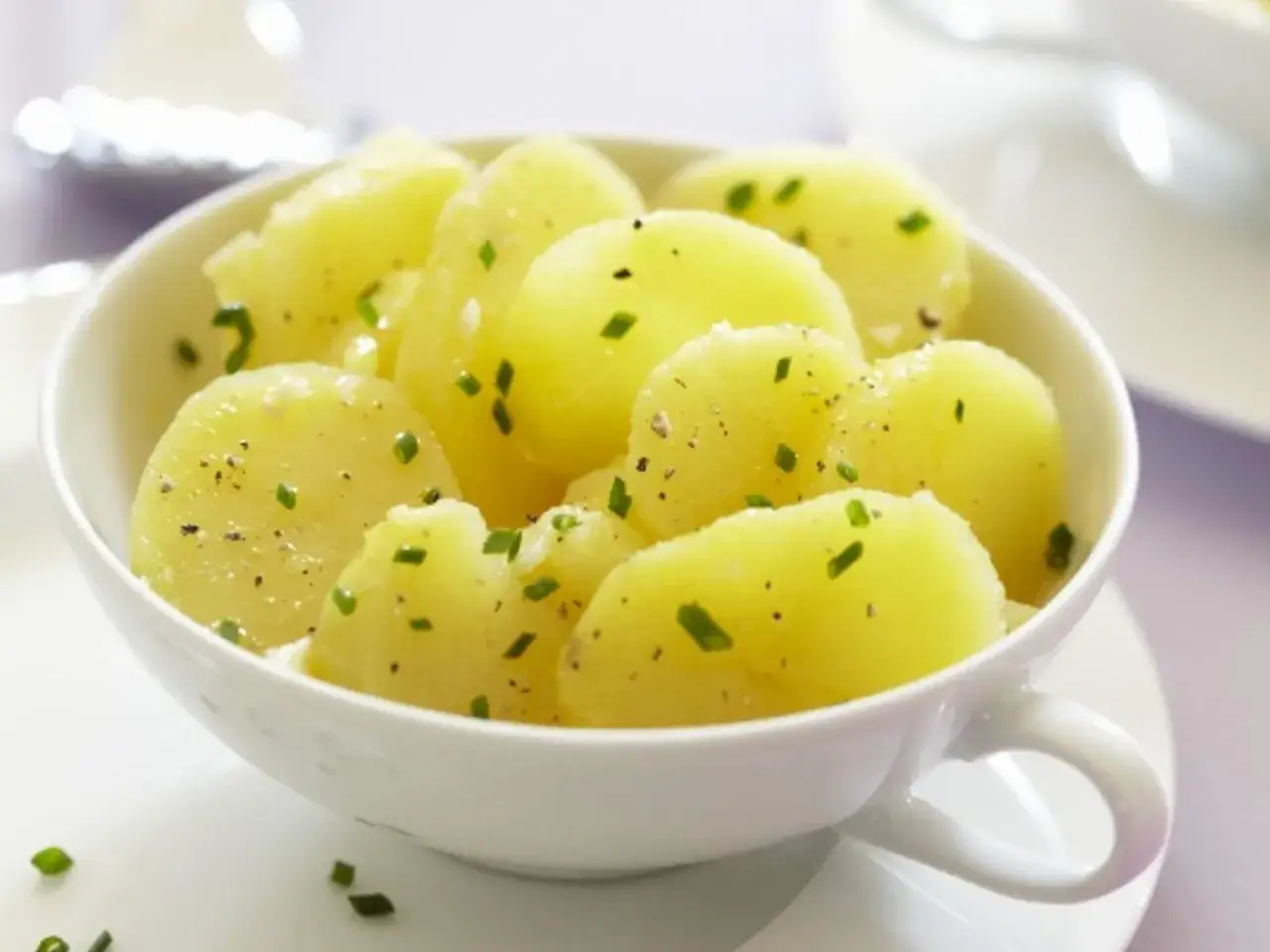 Ein Sch&auml;lchen Kartoffelsalat f&uuml;r 4 Personen, garniert mit frischen Kr&auml;utern und Pfeffer.