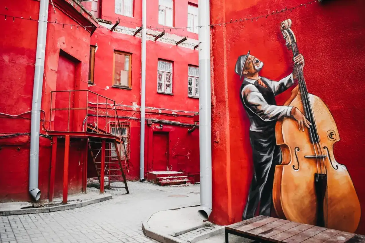 Murale d'un jazzman jouant de la contrebasse dans une ruelle rouge, &eacute;voquant un statut d'artiste libre.