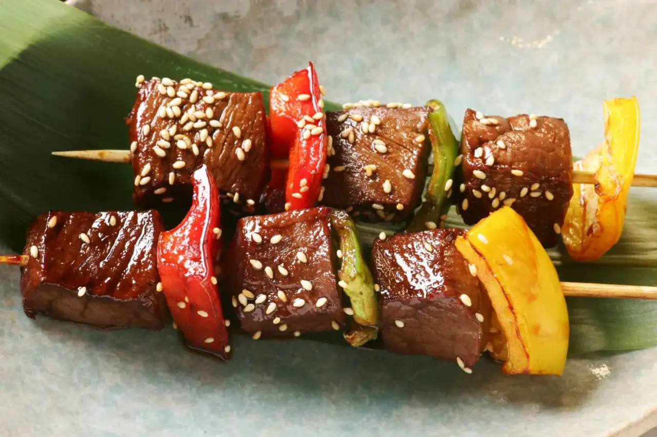 Brochette de rumsteck glacé, parsemée de graines de sésame, avec des morceaux de poivrons rouges, verts et jaunes.