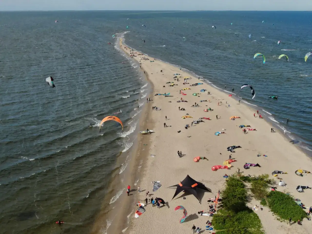 Półwysep w Rewie i okolice to raj dla kitesurferów. Widać tu mnóstwo kolorowych latawców i ludzi cieszących się aktywnym wypoczynkiem na plaży.