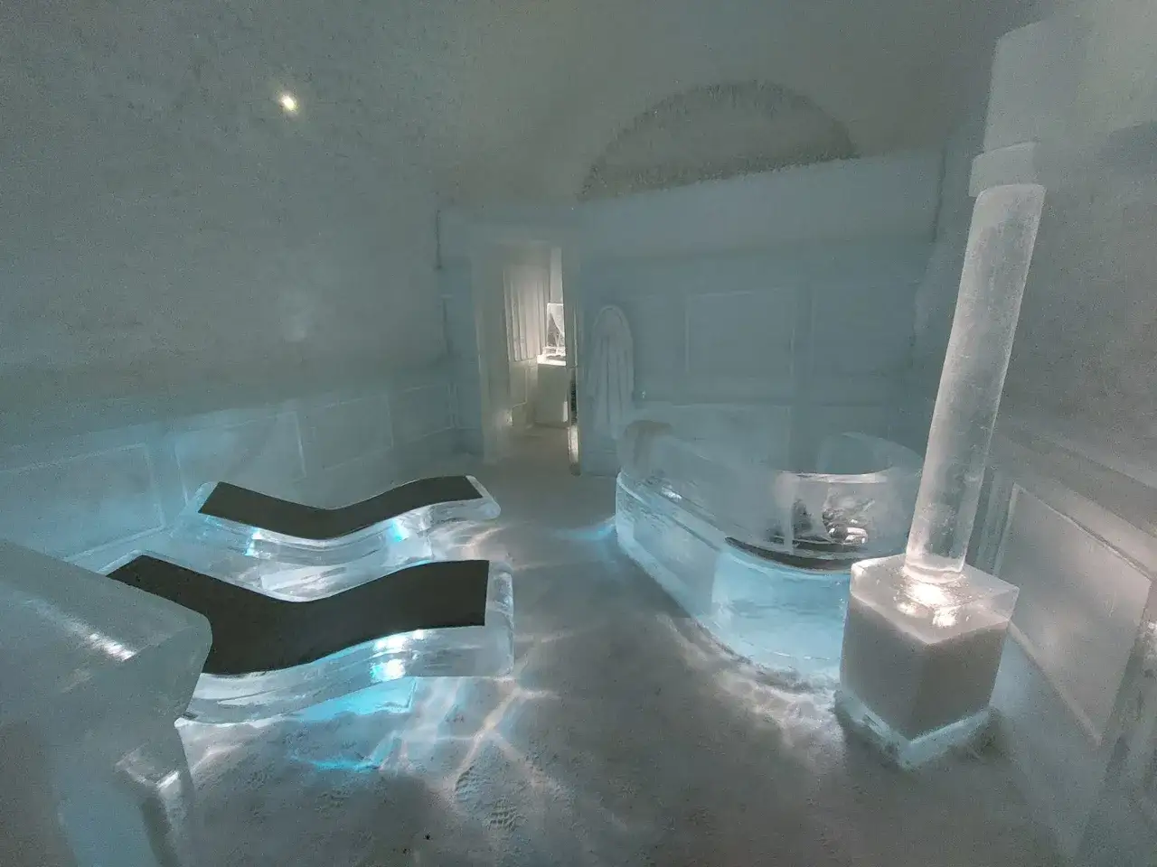Wnętrze hotelu lodowego z lodową wanną i leżakami. Niebieskie światło odbija się od lodu, tworząc magiczną atmosferę.