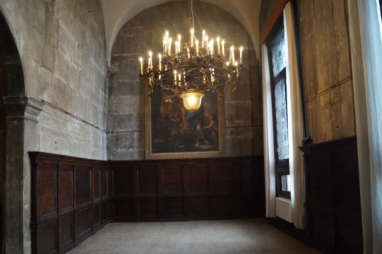 Un antico lampadario illumina una sala con pareti in pietra e boiserie scura, un dipinto e una finestra con vetri piombi a Venezia.