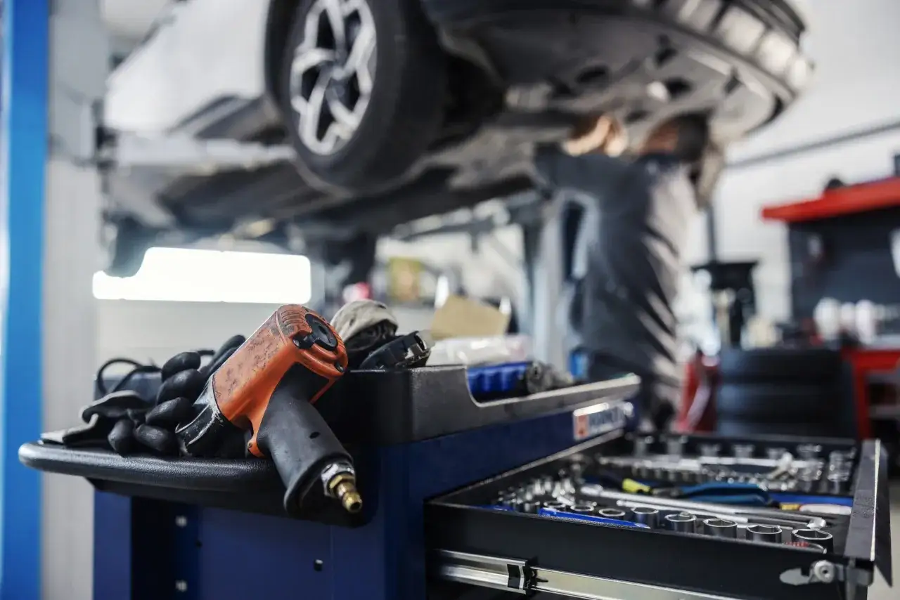 Herramientas listas para el mantenimiento BK Mercedes. Un mec&aacute;nico trabaja en un coche elevado, con una pistola neum&aacute;tica y guantes en primer plano.
