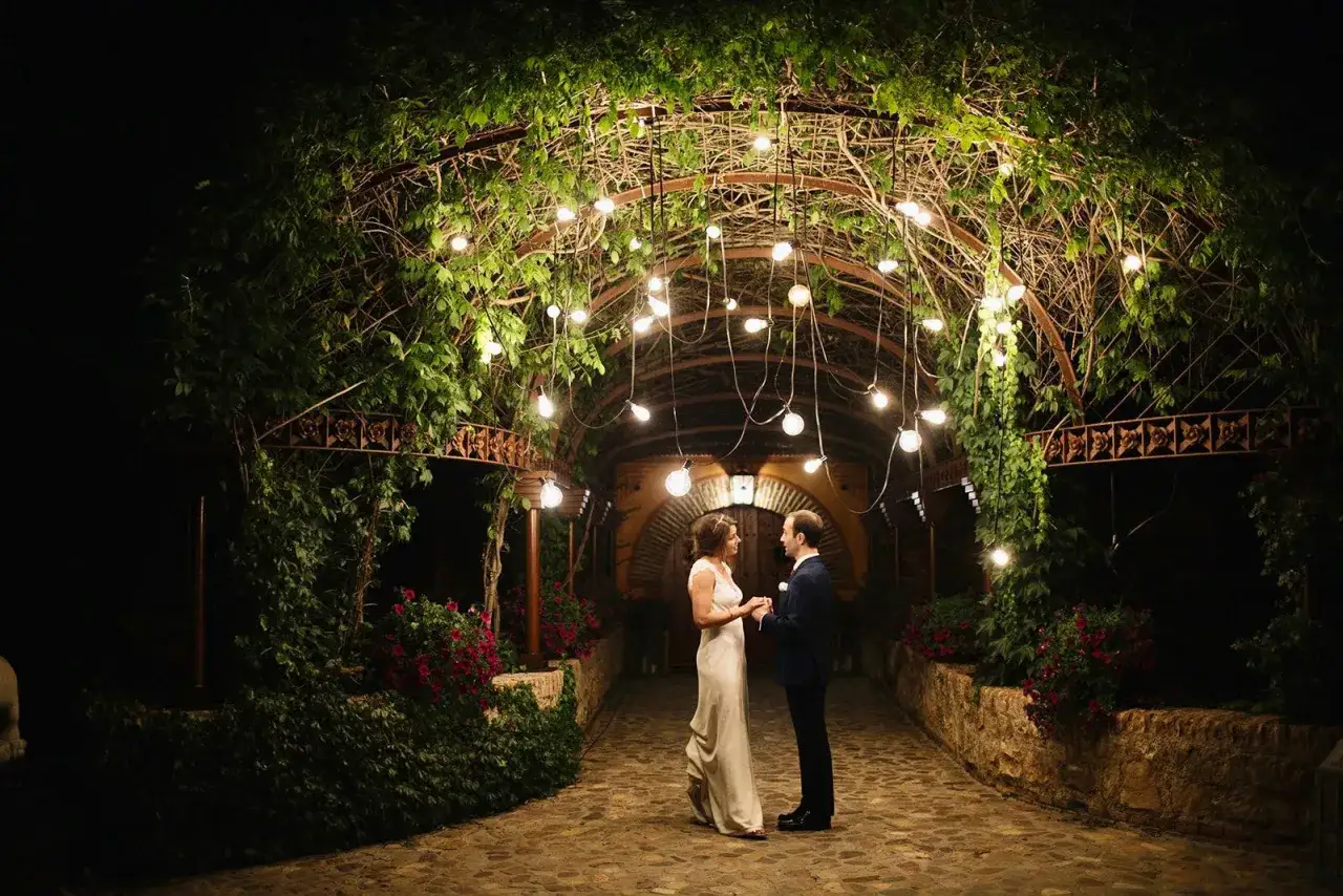 Novios bajo un arco de luces y vegetación, creando un ambiente mágico para su boda tipo coctel.