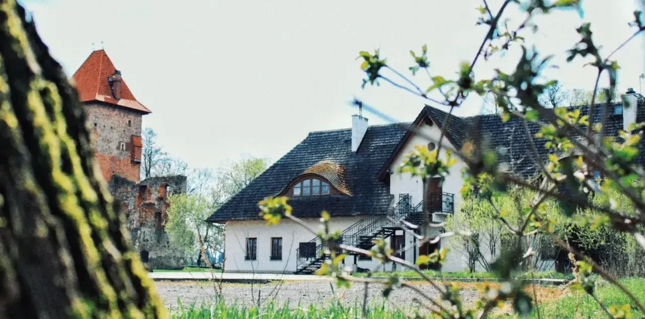 Zamek w Chudowie z wieżą i przylegającym budynkiem, otoczony zielenią.
