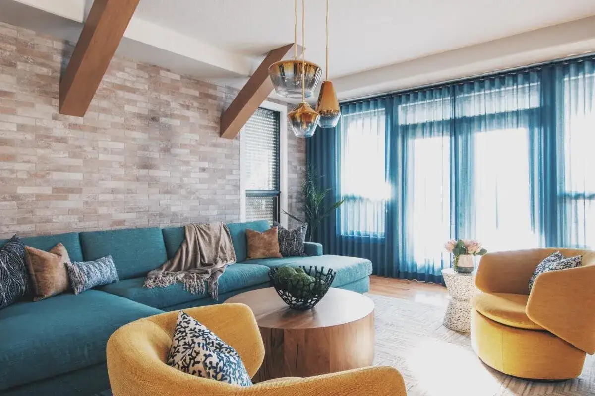 Nowoczesny salon z kanapą w odcieniu cyan blue, ż&oacute;łtymi fotelami i ceglaną ścianą.
