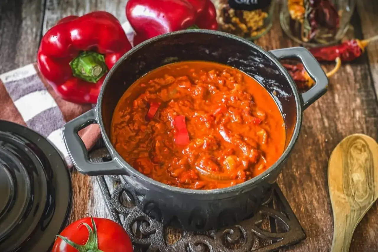 Herzhaftes Zigeunersauce Rezept in einem Gusseisentopf, umgeben von frischen Paprika und Tomaten.