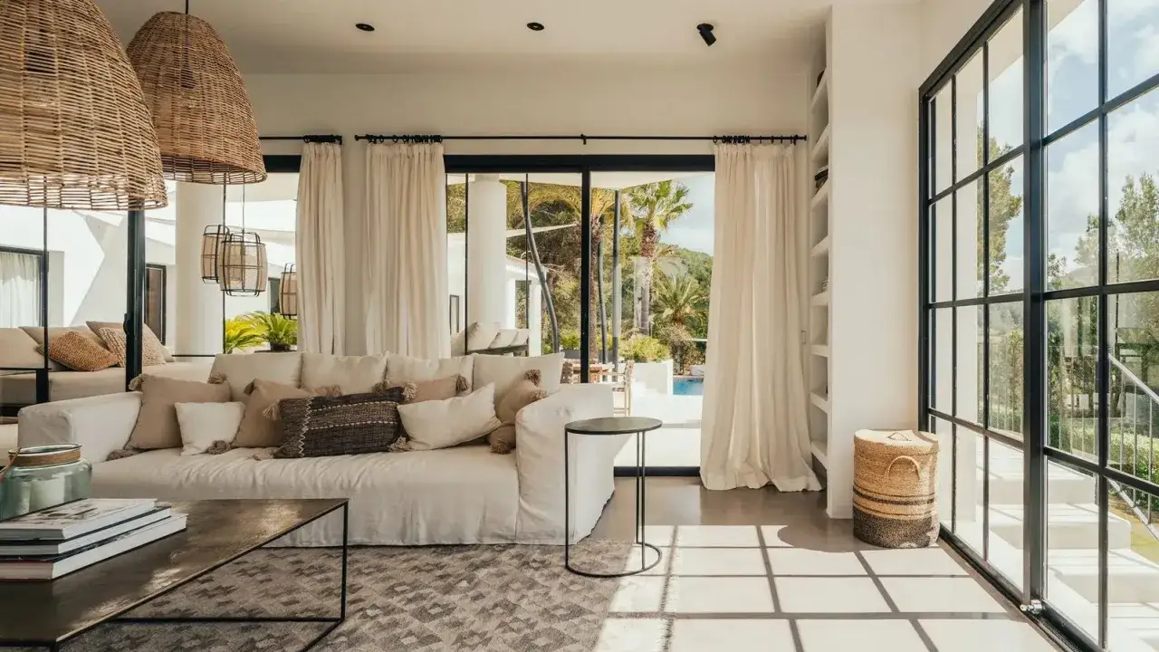 Arredare una casa al mare con divano bianco, cuscini naturali e grandi lampade in rattan. Luce e natura dominano.