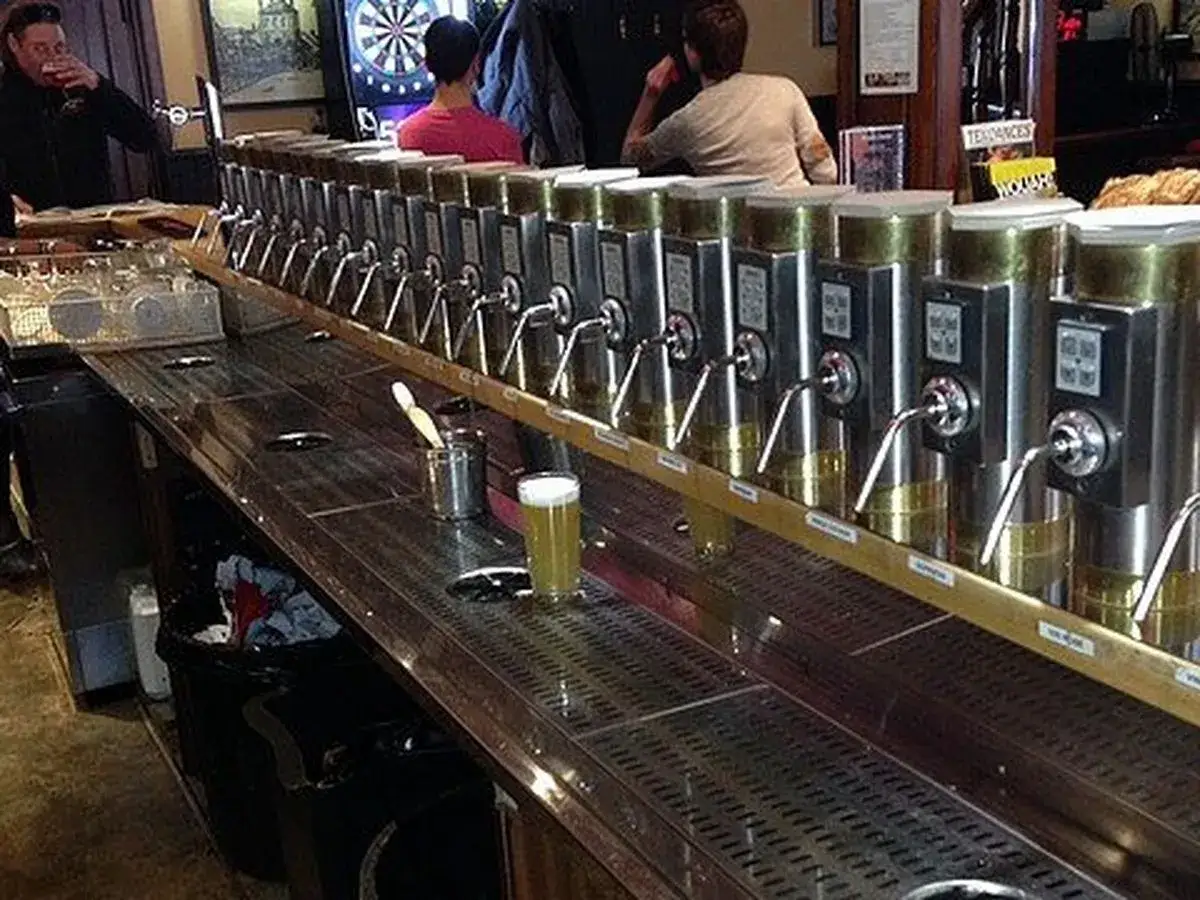 Une rang&eacute;e impressionnante de tireuses &agrave; bi&egrave;re, pr&ecirc;tes &agrave; servir une d&eacute;licieuse cask ale. Un barman boit une bi&egrave;re, un verre de bi&egrave;re est pos&eacute; sur le comptoir.